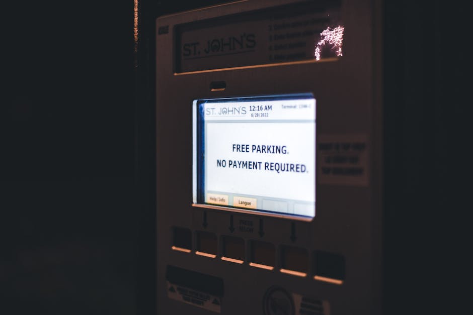 A close-up of a parking meter at night, illuminated by a bright screen displaying the message 'FREE PARKING. NO PAYMENT REQUIRED.' The meter is white with a small digital display and several buttons below the screen, which appears to be glowing softly. The background is dark, with faint reflections possibly from nearby lights, emphasizing the illuminated message on the device. This scene suggests a temporary or special parking arrangement, potentially related to private or alternative waste collection services like those offered by houseclearancestjohnswood.co.uk for rubbish removal and on-site clearance tasks. The absence of other objects or vehicles in the frame keeps the focus solely on the parking meter, providing a neutral, detailed snapshot suitable for accessibility and SEO relevance within a waste management or rubbish disposal context.